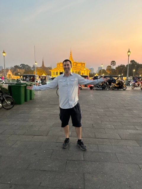 Eric in Phnom Penh Cambodia on the riverwalk in front of golden temple.