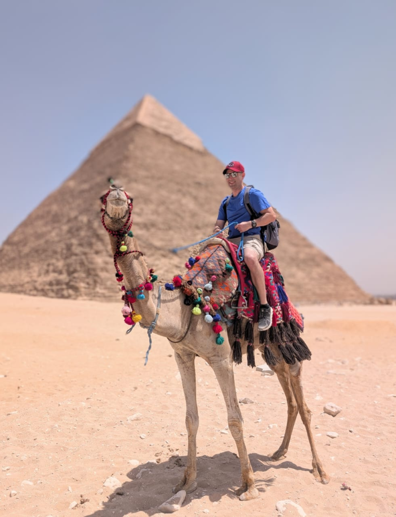 Eric Claggett riding a camel in front of the Pyramids of Giza.