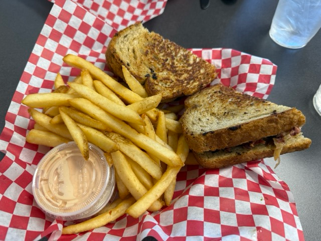 Rueben sandwich with french fries and cup of ranch dressing at an American restaurant.